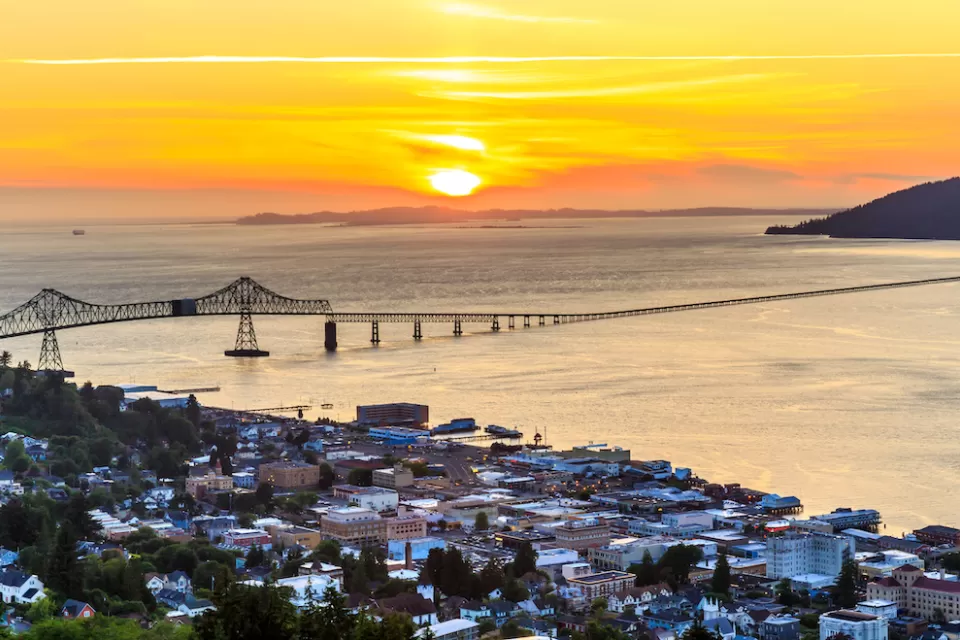 Aerial view of coastal town of Astoria, Oregon with suspension bridge and sunset sky.